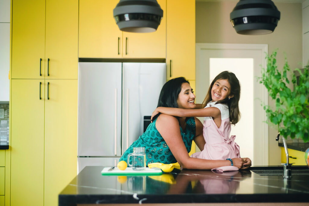South Asian entrepreneur hugging daughter in kitchen